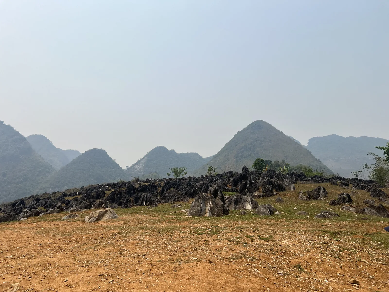 Đá vôi đen lởm chởm rải trên đồi với những núi hình chóp mờ sương phía xa, Điện Biên.