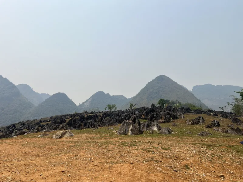 Đá vôi đen lởm chởm rải trên đồi với những núi hình chóp mờ sương phía xa, Điện Biên.